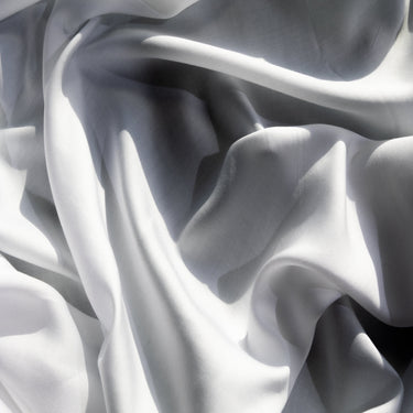 White draped fabric with soft folds and shadows, filling the entire frame. #color_white